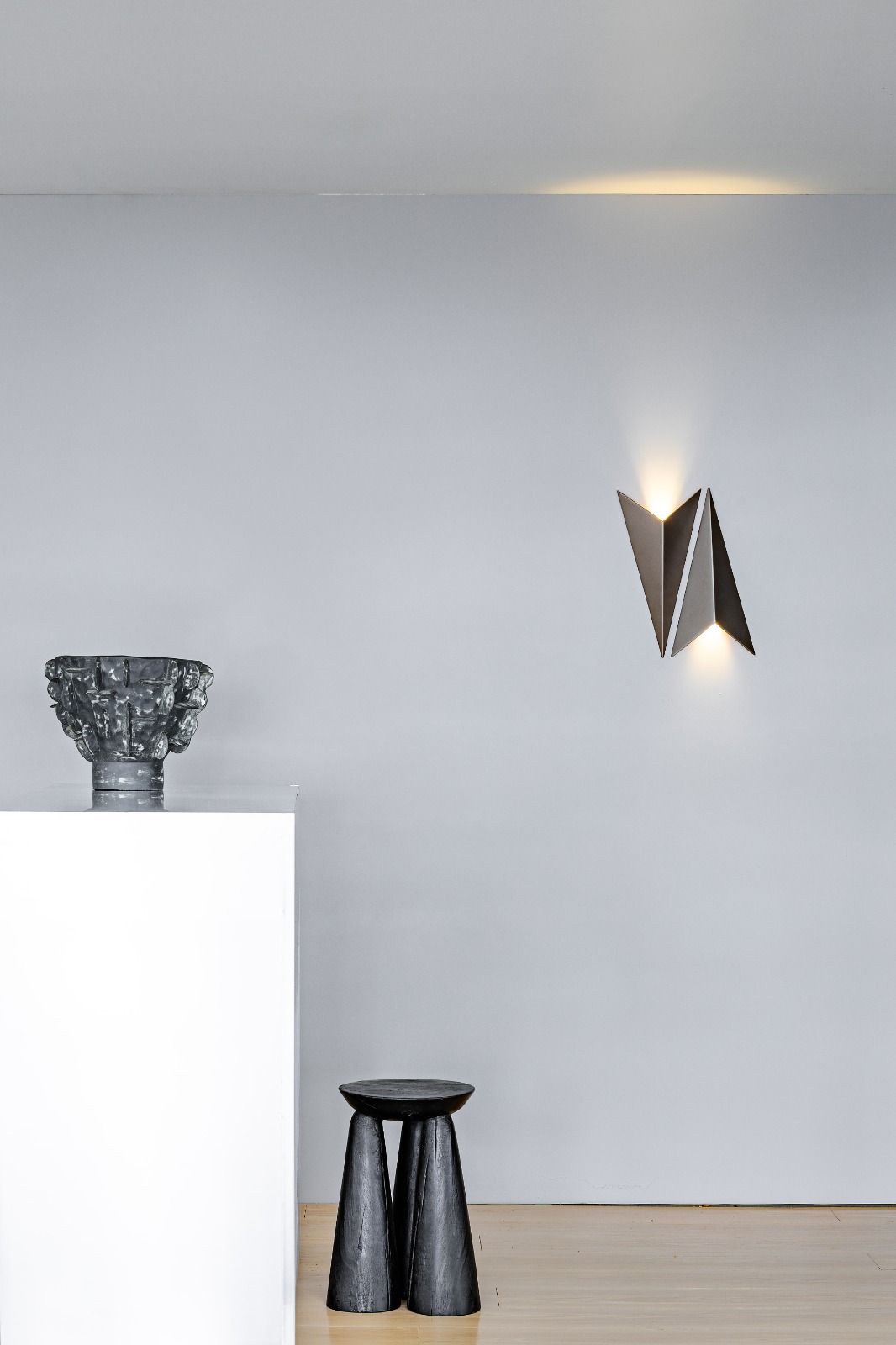 Arandela de LED triangular Avio da Bella Itália instalada na parede, emitindo luz suave, ideal para cabeceira de cama ou lavabos.
